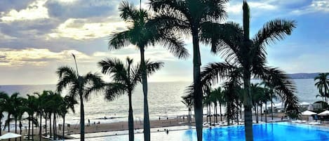 A resort pool area with palm trees, lounge chairs, and umbrellas.