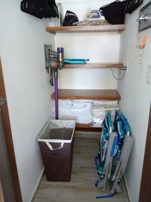 A small storage area with shelves, a vacuum cleaner, and folded items. - Fabulous Presidential Suite with AC and full kitchen  in sunny Nuevo Nayarit (Nuevo Nayarit)