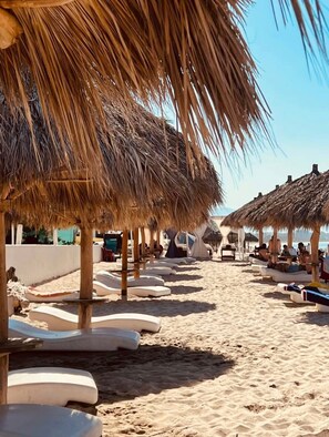 Ein Strand mit Reetsonnenhütten und Liegestühlen.