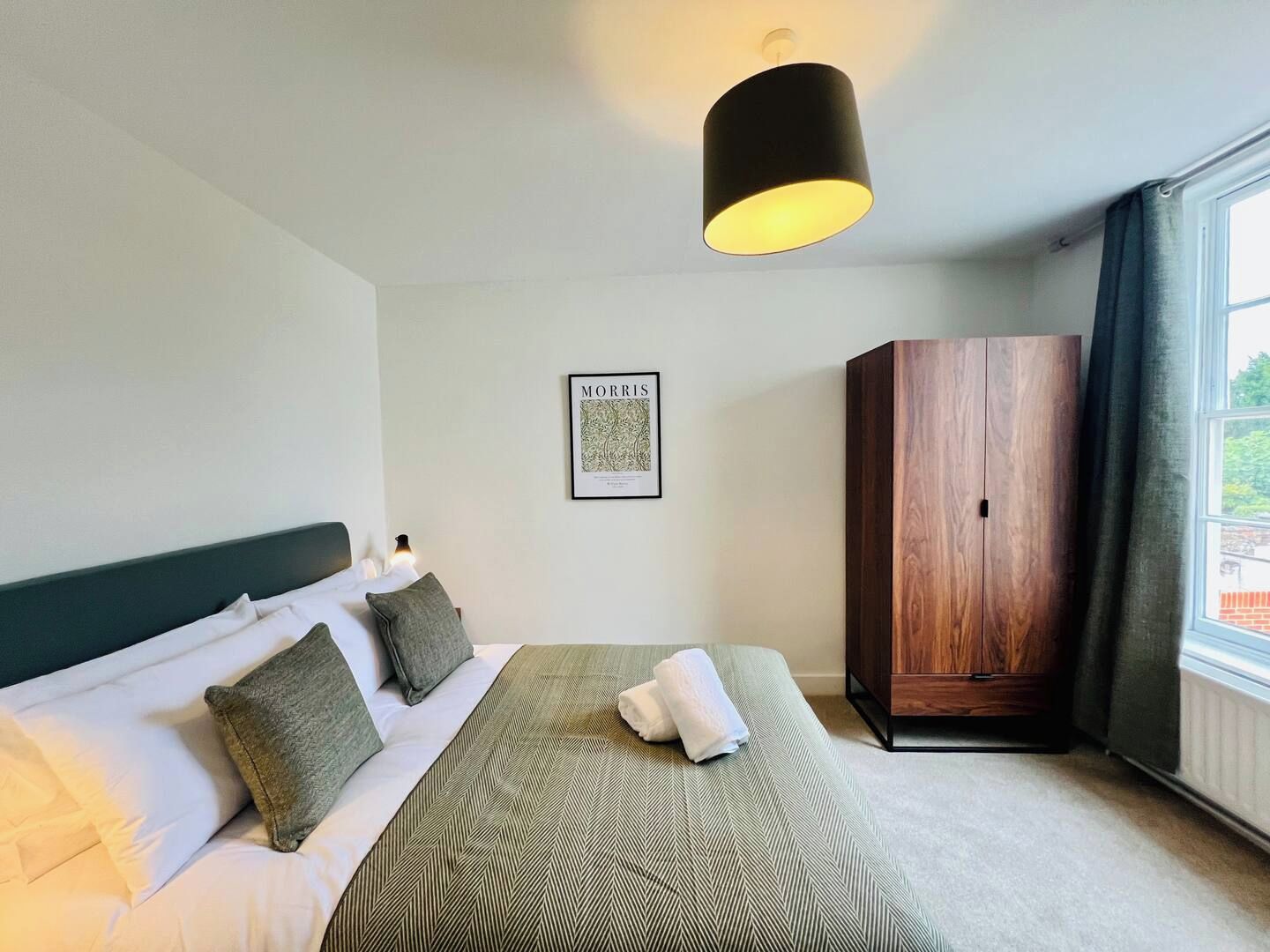 Une chambre d’hôtel avec un lit, une armoire, un tableau encadré au mur et une fenêtre avec des rideaux.