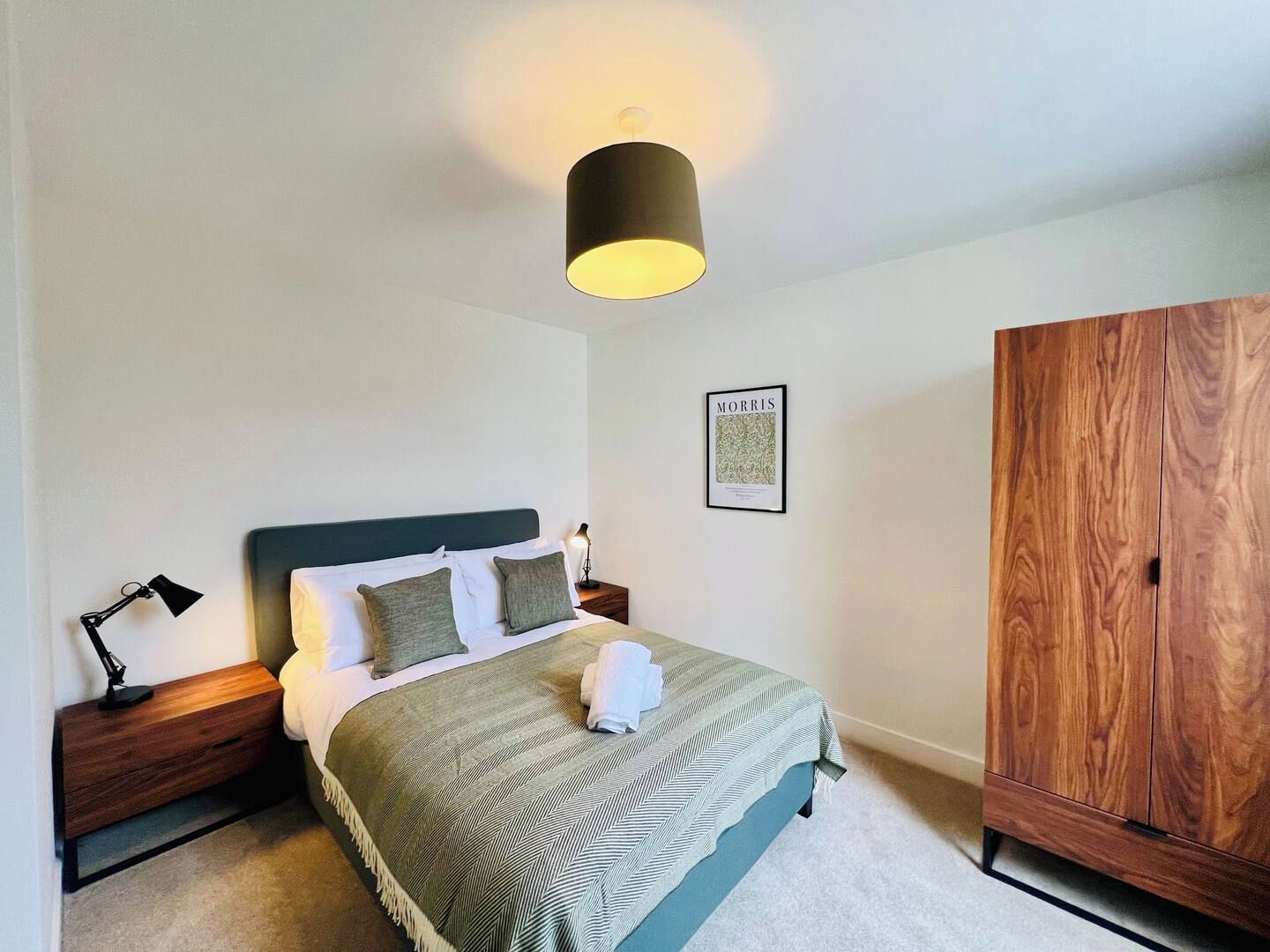 Una camera da letto con un letto, lampade da comodino, una lampada a parete, un quadro incorniciato e un armadio in legno.