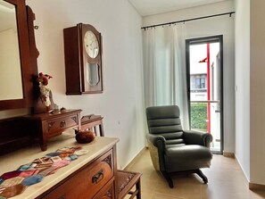 A room with a wooden dresser, a clock, a chair, and a window with curtains.