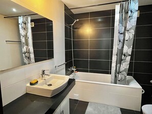 A modern bathroom with a white sink, black tiles, and a shower curtain with a leaf pattern.