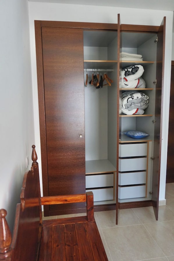 A wooden wardrobe with a sliding door, a bench, and a shelf with folded clothes and a blue dish.