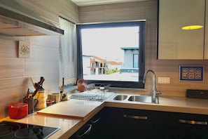 A modern kitchen with a large window, stainless steel appliances, and a view of a residential area.