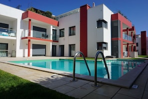 A modern building with a swimming pool, balconies, and a clear sky.