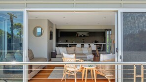 Ein modernes Wohnzimmer mit Glasbalkon, Essbereich und sichtbarer Küche durch die Scheiben.