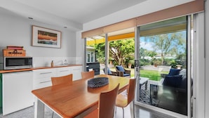 Una cucina moderna con zona pranzo, porte scorrevoli in vetro che si aprono su un giardino con mobili da esterno.