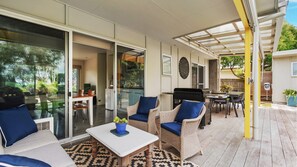 Ein überdachter Patio-Bereich mit Gartenmöbeln, einem Grill und Blick auf den Garten.