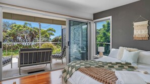 Ein Schlafzimmer mit Bett, Nachttisch, Lampe, Fenster und einem Balkon mit Stuhl.