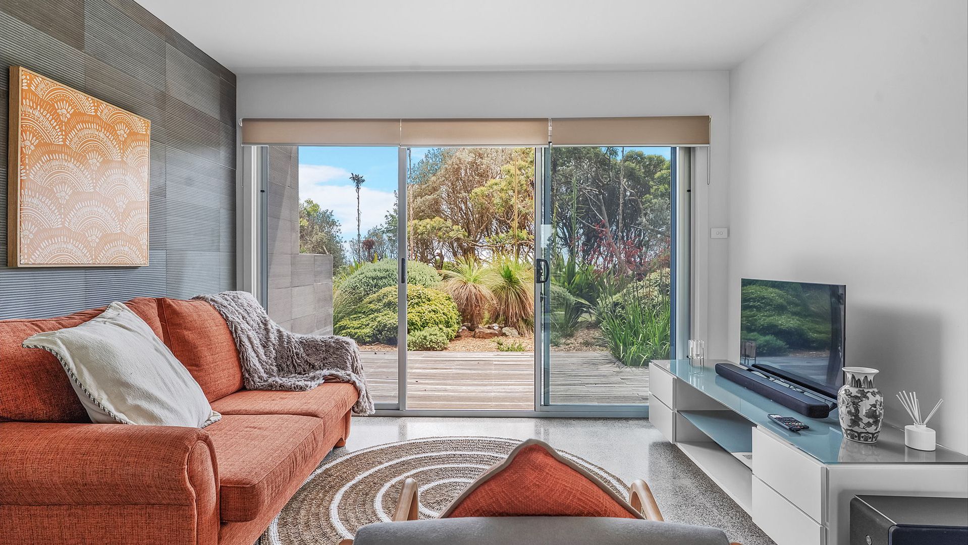 A modern living room with a sliding glass door leading to a garden, a sofa, a TV, and a coffee table.