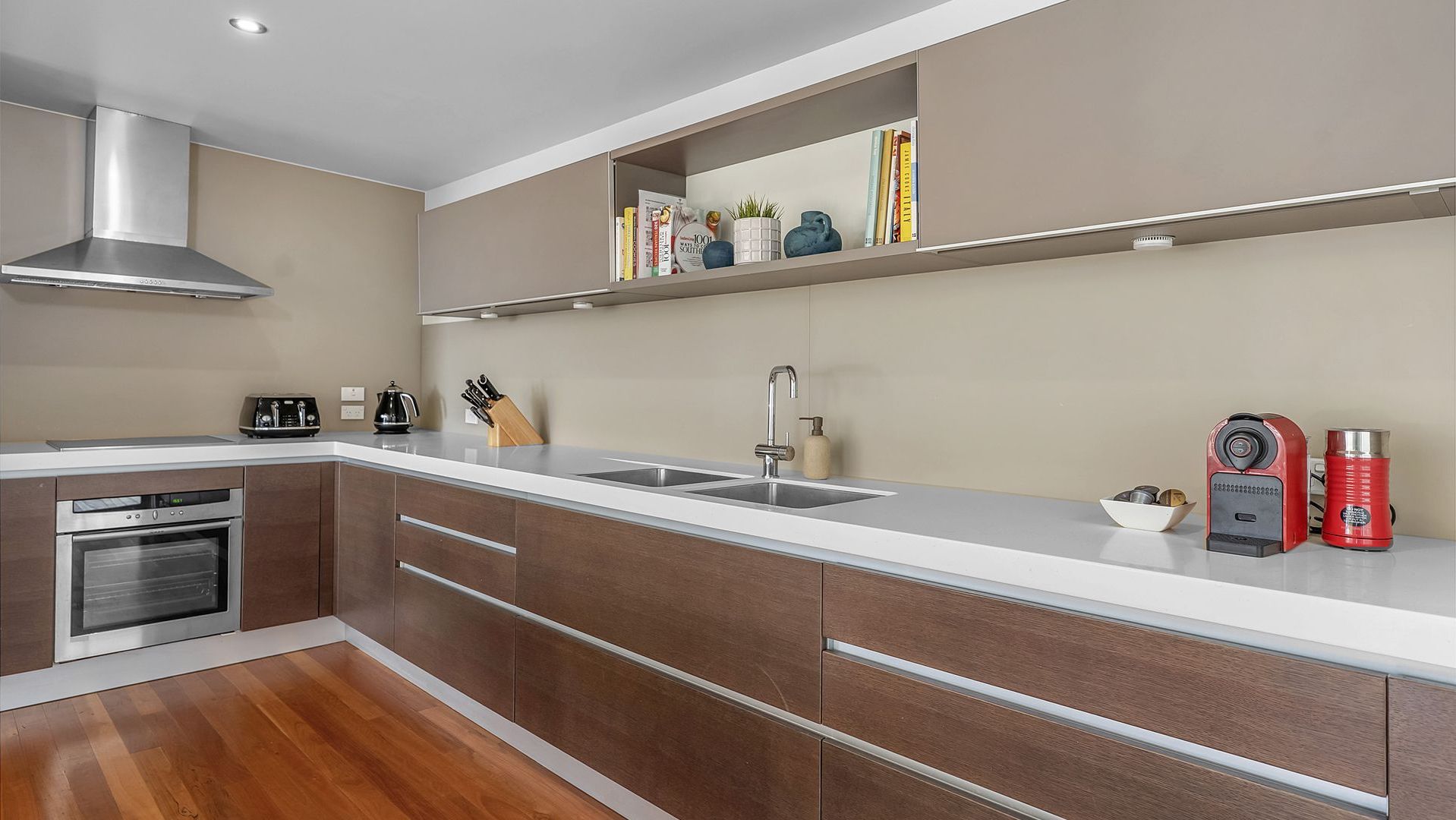 A modern kitchen with a built-in oven, a stainless steel range hood, a double sink, and a coffee machine.