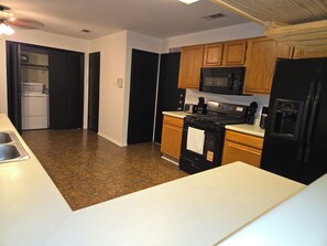 A kitchen with a microwave, stove, refrigerator, and a washing machine in the adjacent room. - Beautiful Austin Home | Spacious, Furnished & Comfortable (Austin)