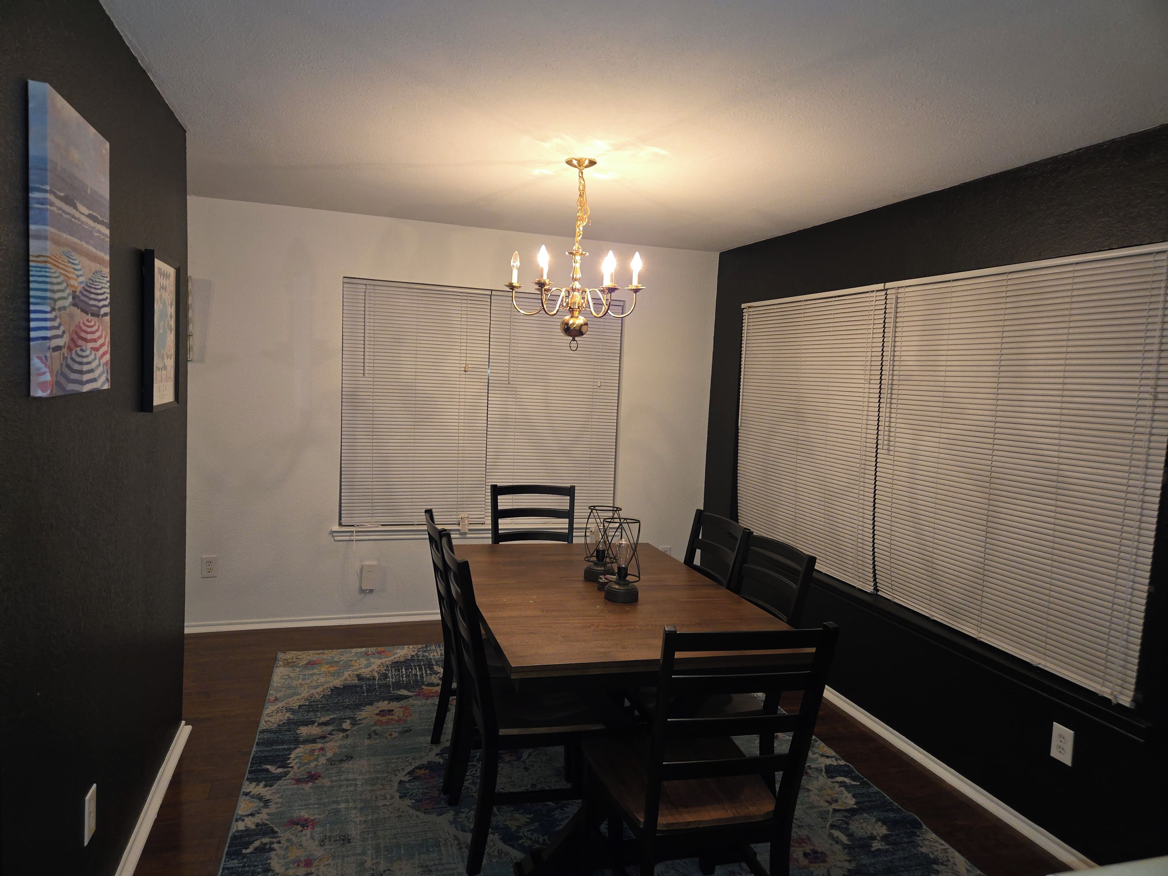 A dining room with a wooden table, black chairs, a chandelier, and a patterned rug.