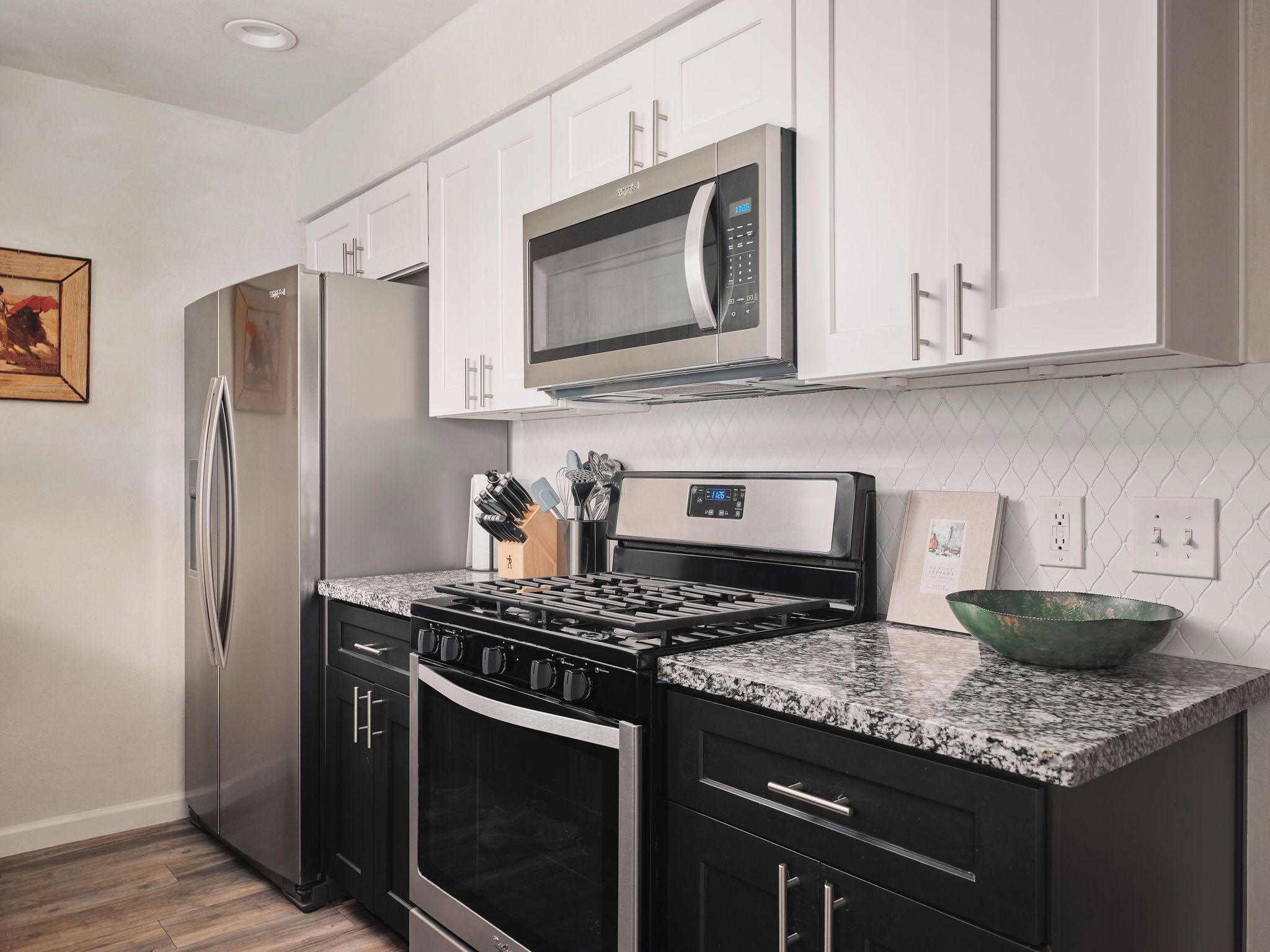 A modern kitchen with stainless steel appliances, white cabinetry, and a granite countertop.