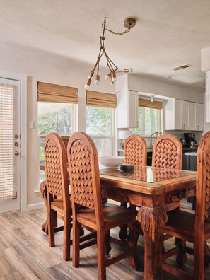A dining area with a wooden table and chairs, a hanging light fixture, and a view of the kitchen through the open door. - Casa Peña | Designer 3BR Retreat w/ Fire Pit (Austin)