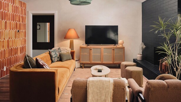 Ein Wohnzimmer mit einer Couch, einem Fernseher, einer Lampe und einer Pflanze.