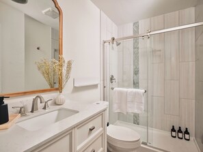 A modern bathroom with a white sink, mirror, and shower. - Casa Peña | Designer 3BR Retreat w/ Fire Pit (Austin)