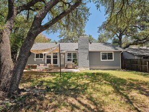 A residential house with a patio area, a barbecue grill, and a stone chimney. - Casa Peña | Designer 3BR Retreat w/ Fire Pit (Austin)