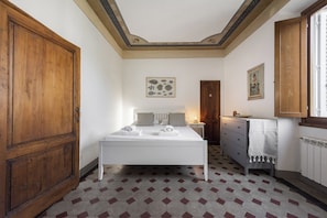 Un dormitorio con un amplio armario de madera, una cama con ropa blanca, un aparador y una pared decorada con dos obras enmarcadas.