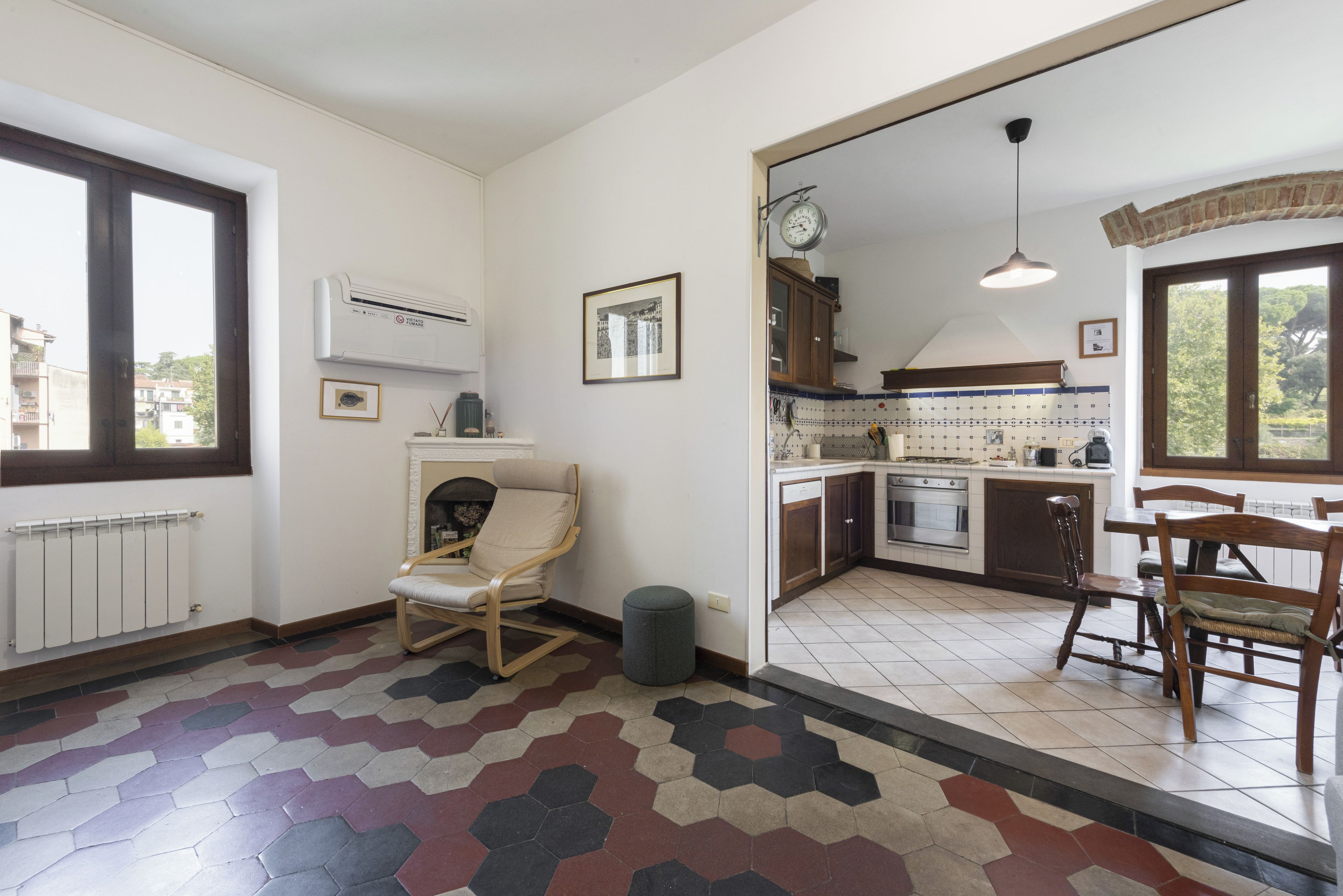 A spacious living area with a fireplace, a dining table with chairs, a kitchen with a stove and cabinets, and a large window.