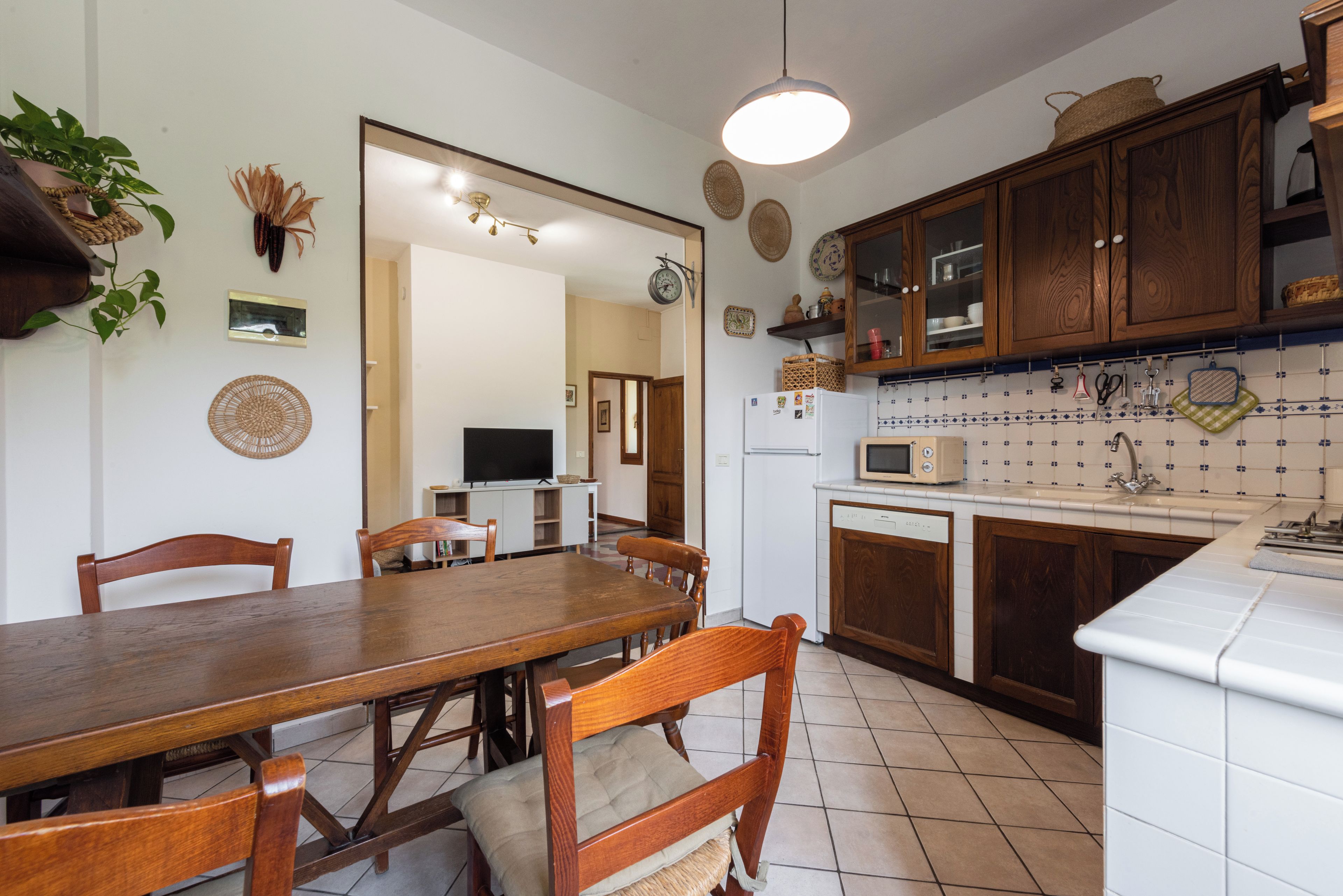 Una cocina con armarios de madera, una mesa de comedor con sillas, un microondas y un refrigerador.