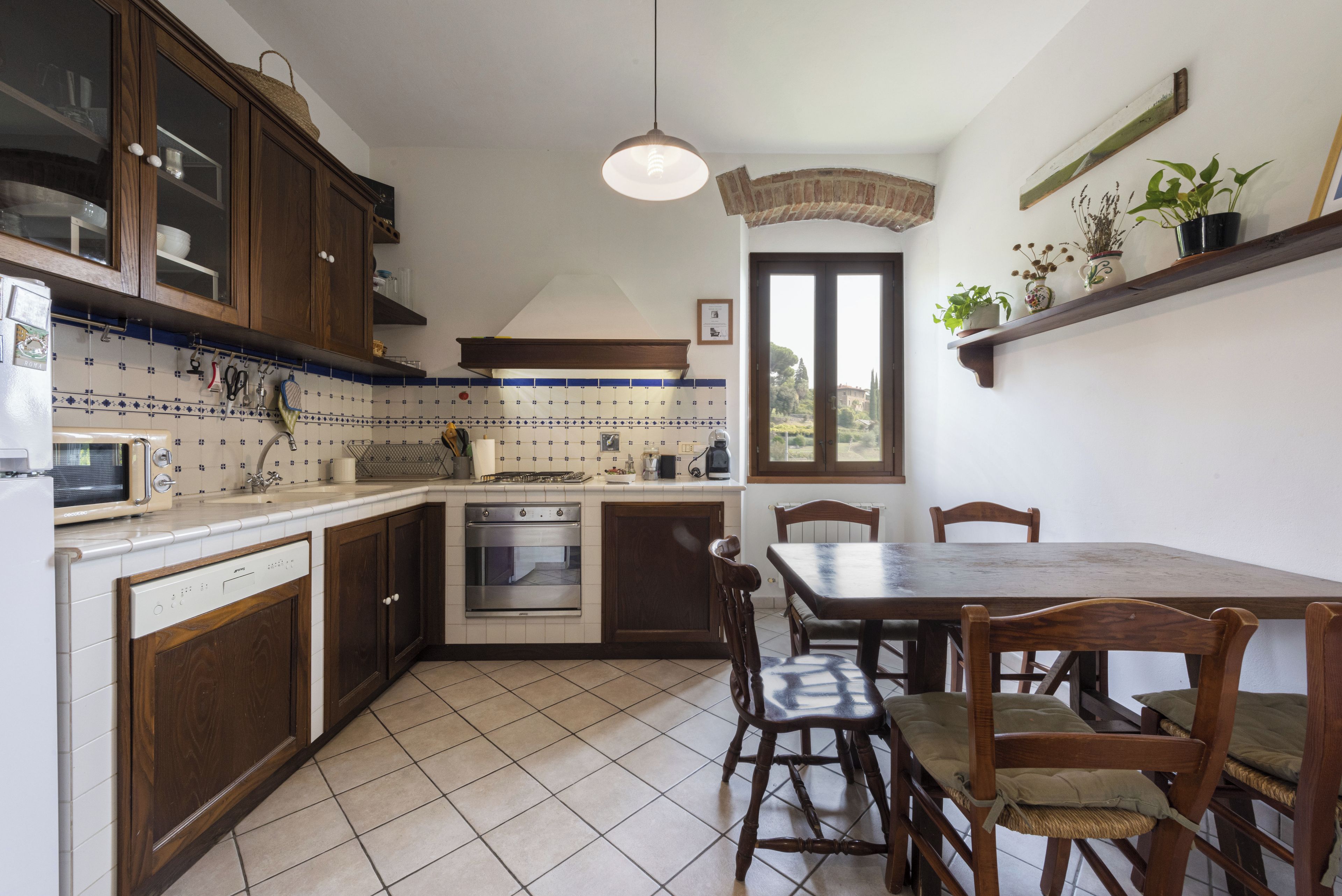 A kitchen with wooden cabinets, a built-in oven, a dining table with chairs, and a hanging light fixture.