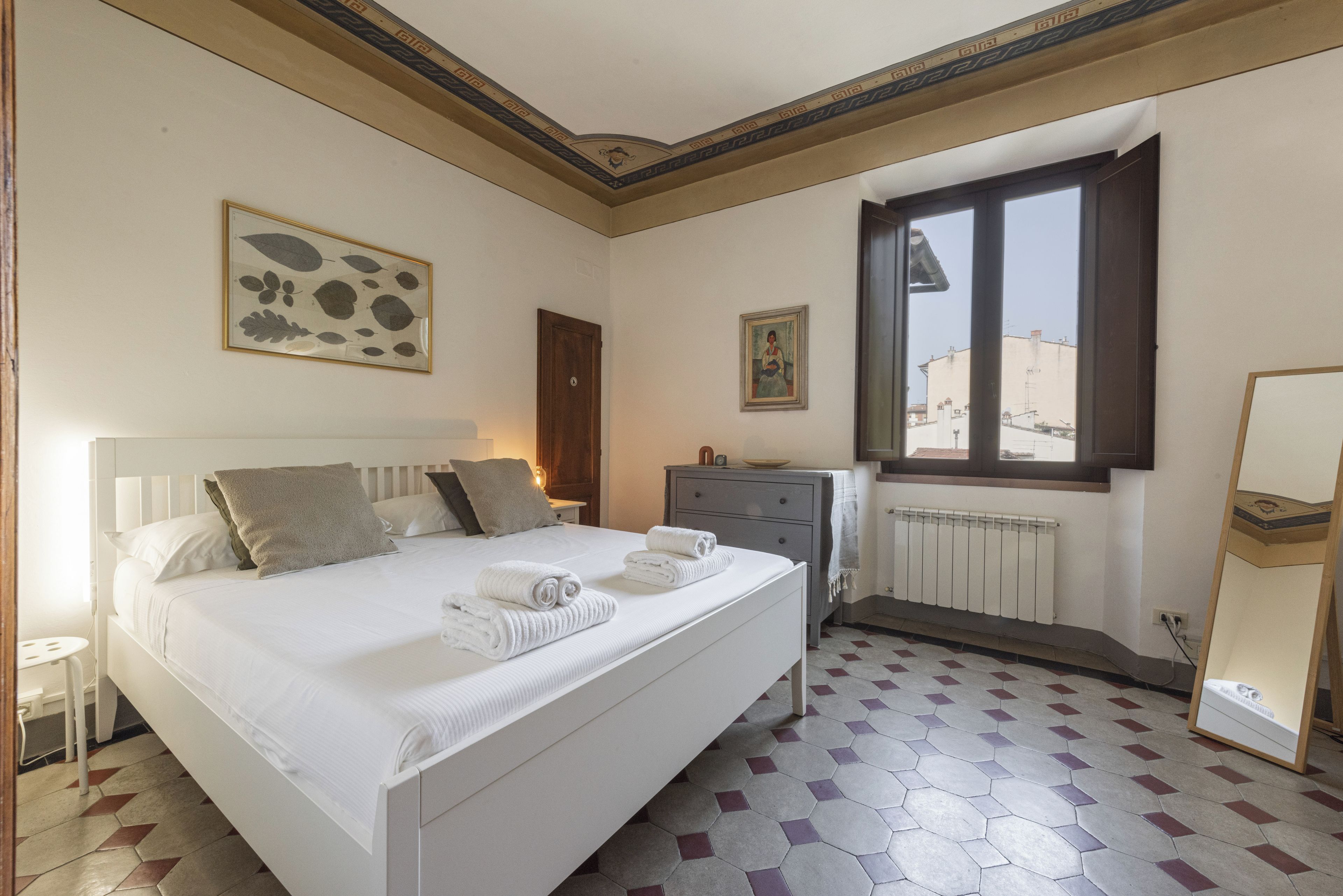Habitación de hotel con cama, cómoda, ventana con vista y un cuadro en la pared.