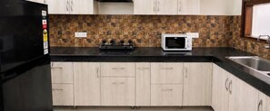 A kitchen with light wood cabinets, a black countertop, a stove, and a microwave.