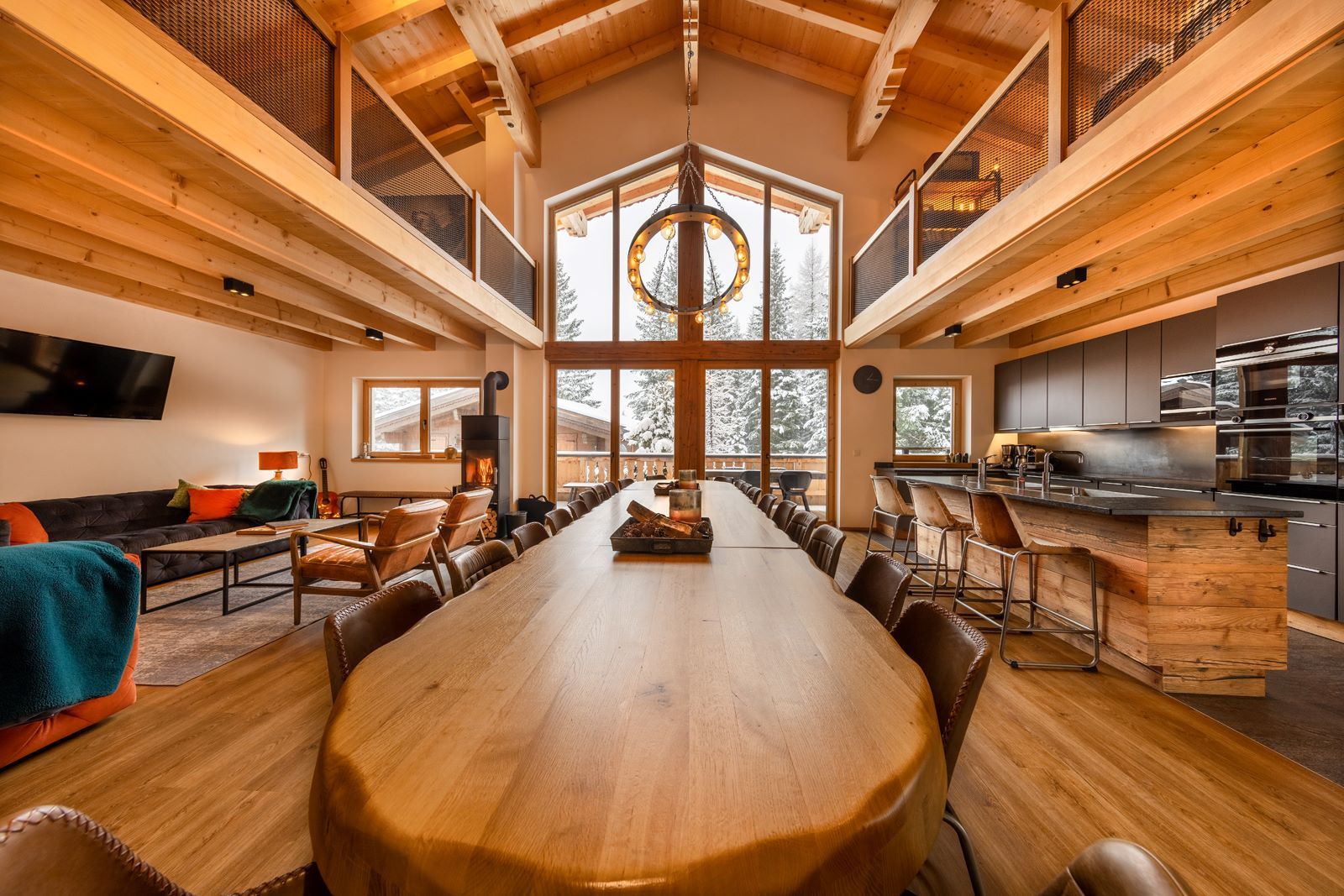 A spacious room with a long wooden table, multiple chairs, a fireplace, and a kitchen area.