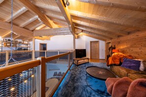 An attic room with a wooden ceiling, a television, a sofa, and a small table. - Superb 9-bedroom chalet in alpine Zillertal for your getaway or wintersports (Hochkrimml)