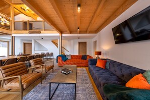 A spacious living area with a high ceiling, a large flat-screen TV mounted on the wall, and a cozy seating arrangement including a sofa and chairs. - Superb 9-bedroom chalet in alpine Zillertal for your getaway or wintersports (Hochkrimml)