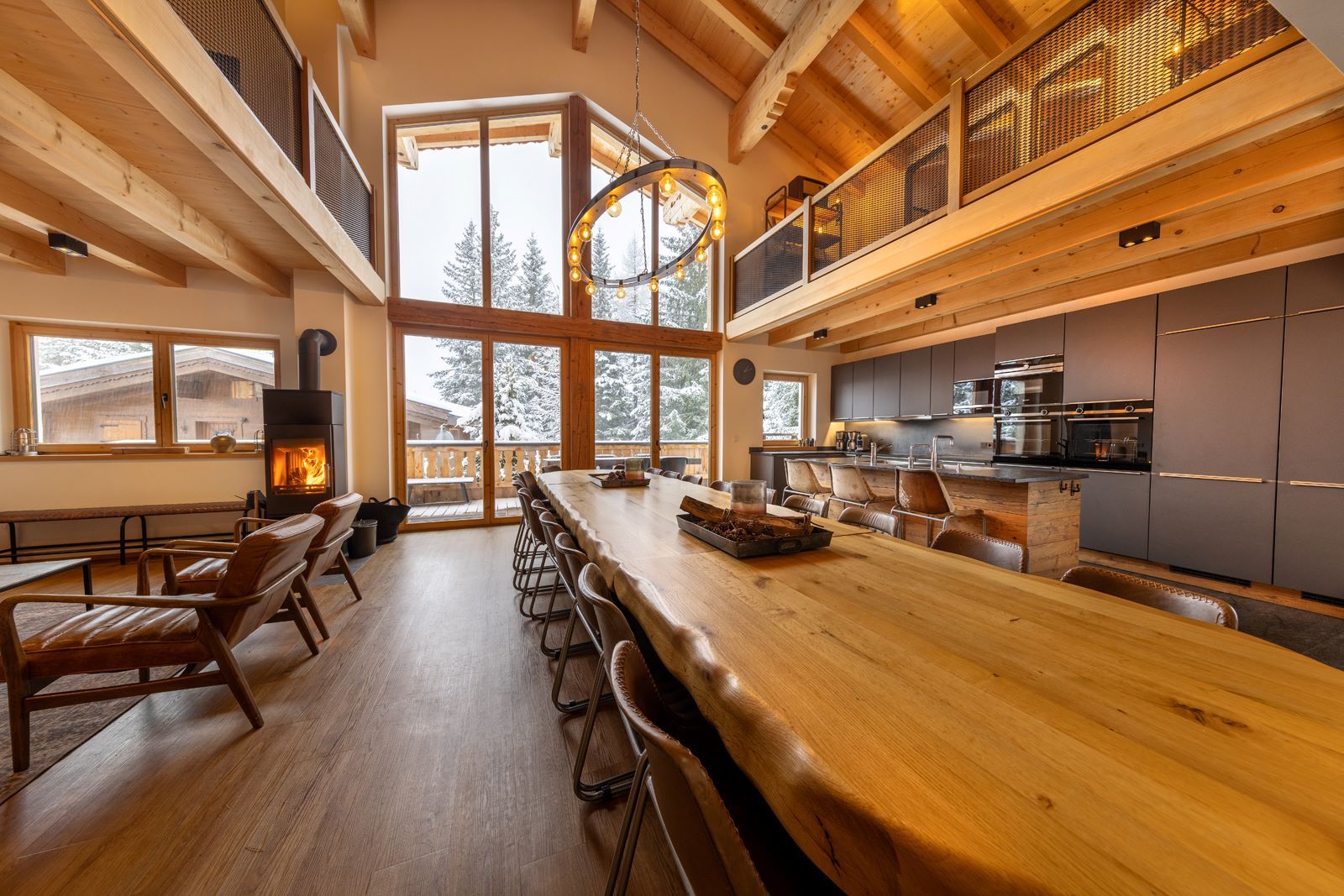 A spacious room with a long wooden table, multiple chairs, a fireplace, and a kitchen area.