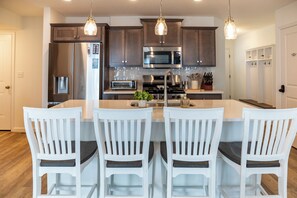 Una cocina moderna con una isla central, sillas blancas e iluminación colgante.
