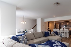 Ein modernes Wohnzimmer mit einer Couch, einem Esstisch und Stühlen. Es gibt eine Küchenzeile mit Schränken und einer Mikrowelle.