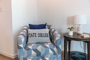 A chair with a geometric pattern and a pillow with 'STATE COLLEGE' text, a small table with a lamp and a plant, and a glass tray on the table. - Welcome to Happy Valley Retreat! Features a golf simulator and a game room! (Bellefonte)