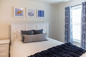 Ein Schlafzimmer mit einem weißen Bettkopfs, einem Bett mit grau-weißen Kissen und drei gerahmten Kunstwerken an der Wand.