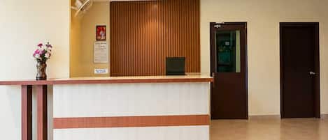 A reception desk with a wooden panel backdrop, a wall-mounted fan, and a door to the right.