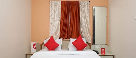 Habitación de hotel con una cama, dos almohadas rojas, una mesita de noche y un espejo.