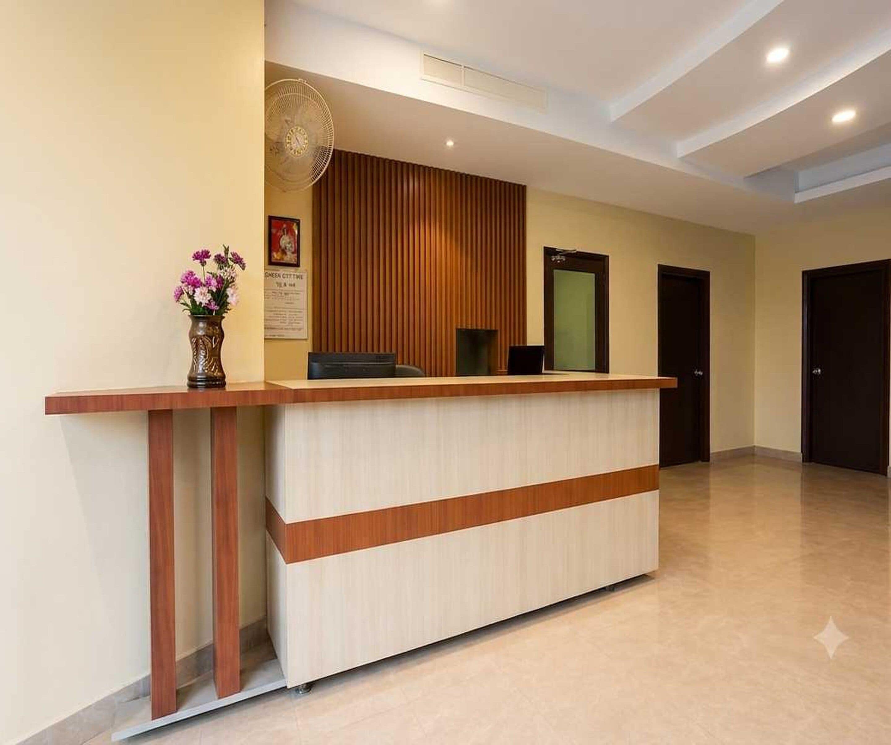 A reception desk with a wooden finish, a vase with flowers, and a wall-mounted fan.