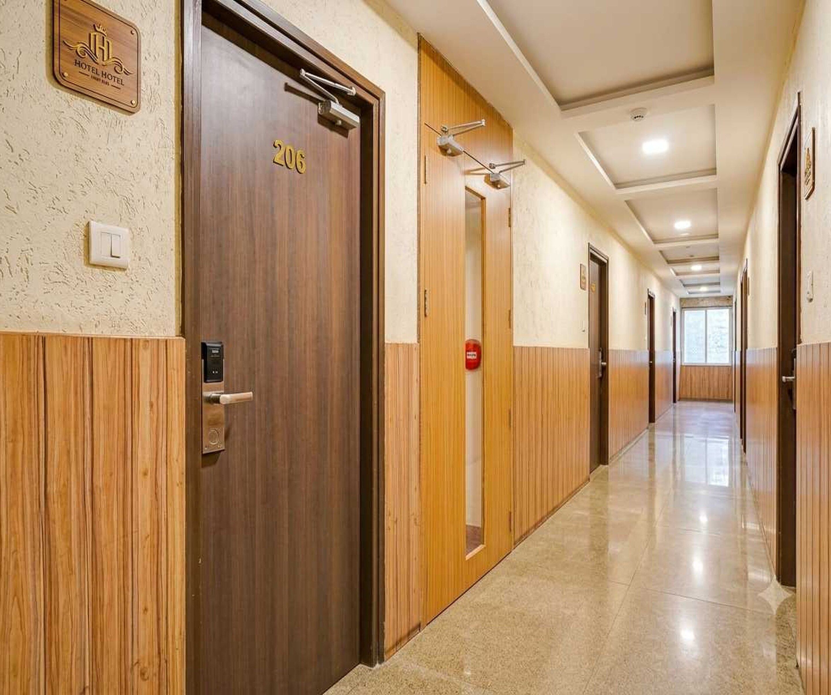 A hotel corridor with wooden doors, a fire alarm, and a light switch on the wall.