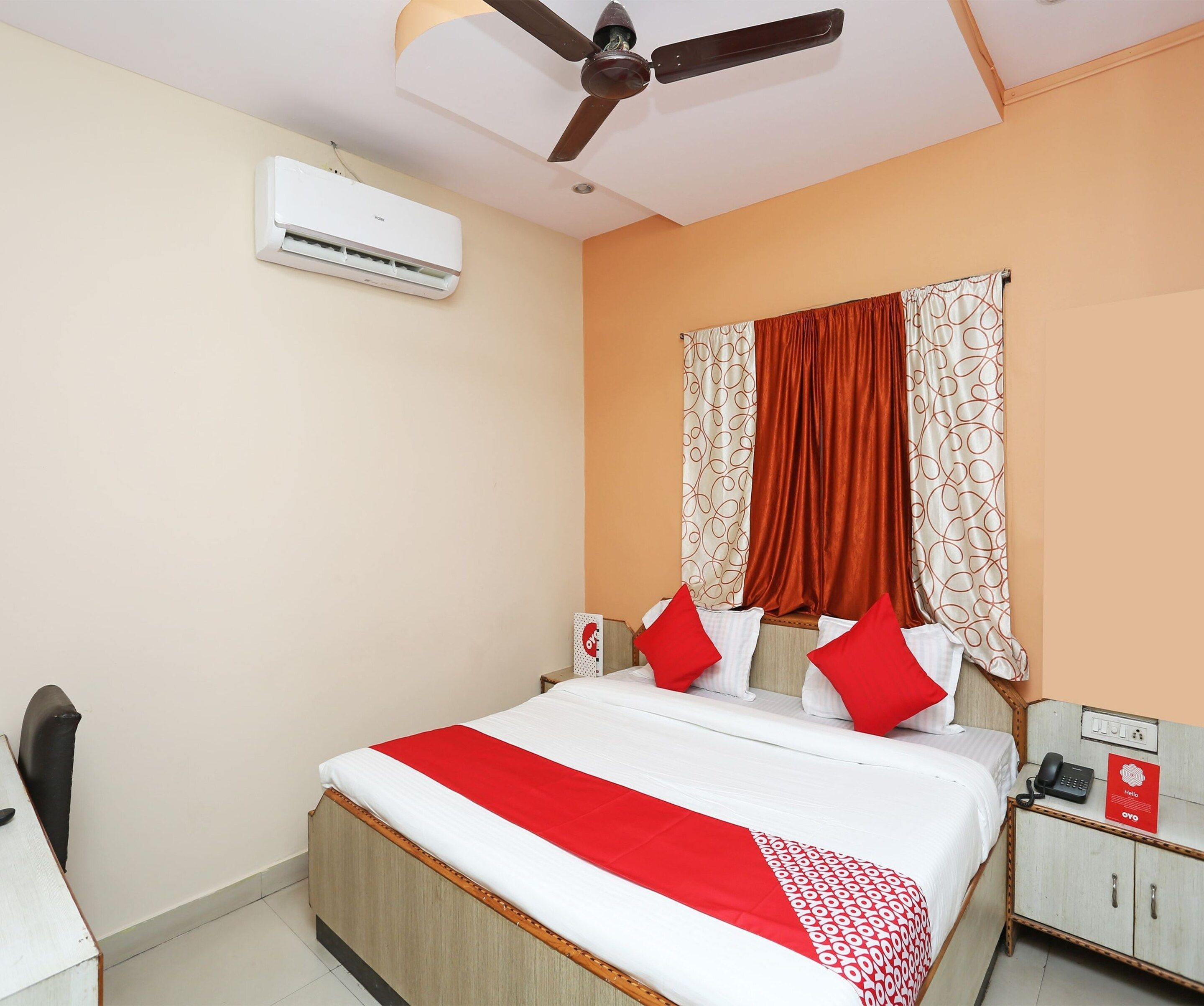 A hotel room with a bed, a desk, a telephone, and an air conditioning unit.