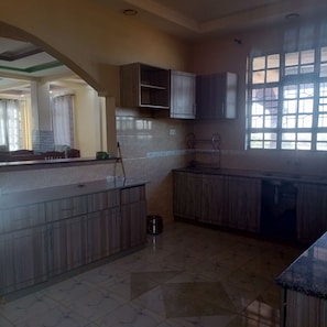 Una cocina con piso de mármol, gabinetes de madera, una encimera y un ventanal con diseño de cuadrícula.