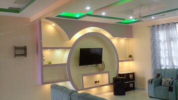 A modern living room with a large TV, a sofa, and a ceiling with green lighting accents.