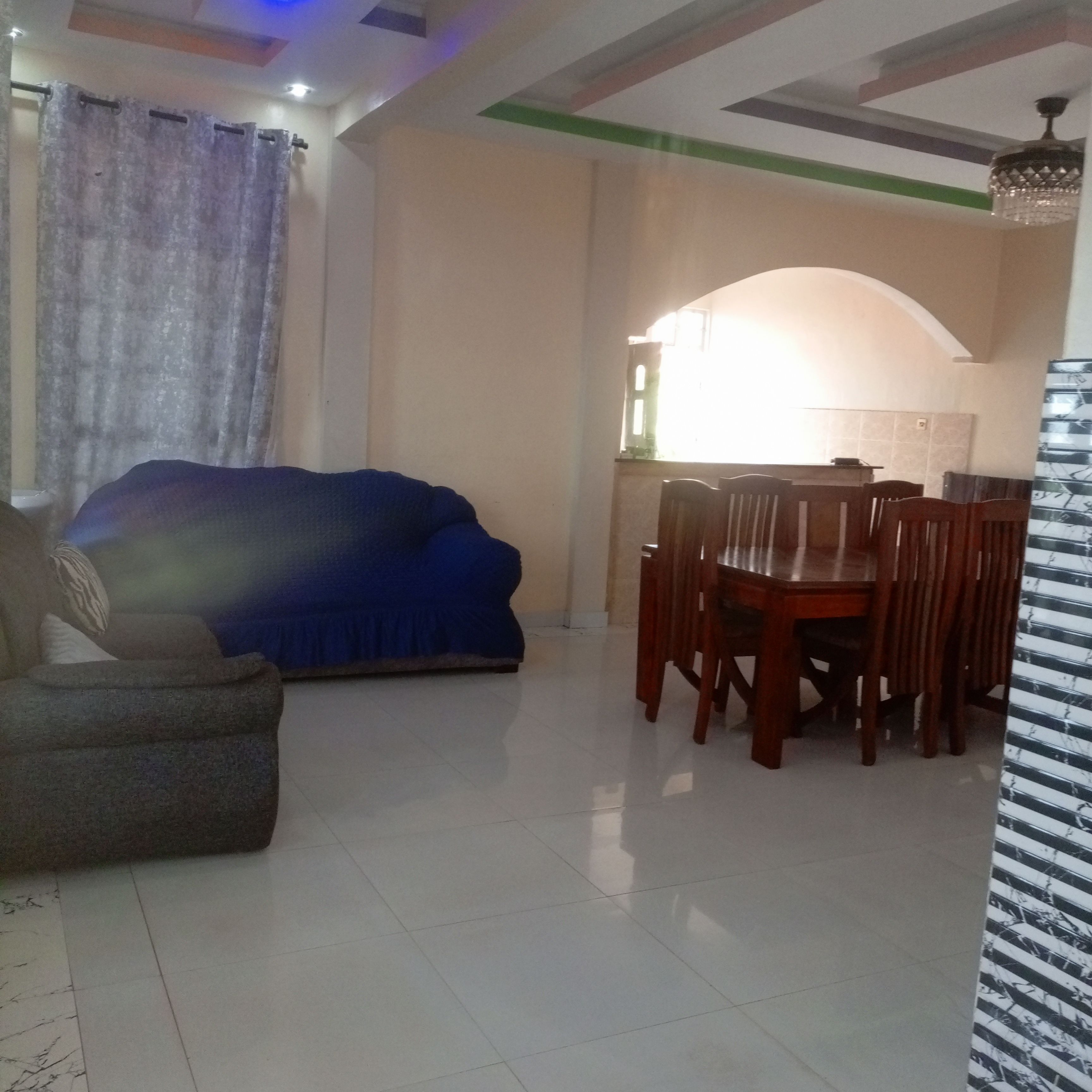 Sala de estar com sofá, mesa de jantar e cadeiras, e área de cozinha ao fundo.