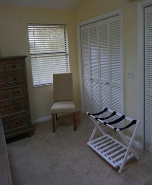 A room with a wooden dresser, a chair, a white bench with black straps, and a closet with white louvered doors. - COMPLETELY RENOVATED! Newly furnished 2 bedroom condo in the heart of St. Simons (St. Simons Island)