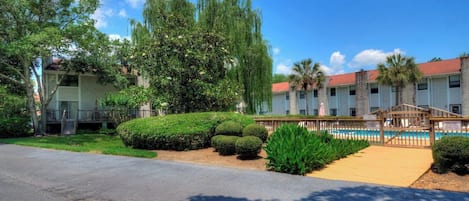 A hotel with a swimming pool, a covered patio, and a well-maintained garden with various shrubs and trees.