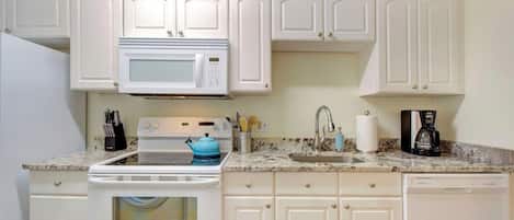 Una cocina con armarios blancos, microondas, estufa, fregadero y cafetera.