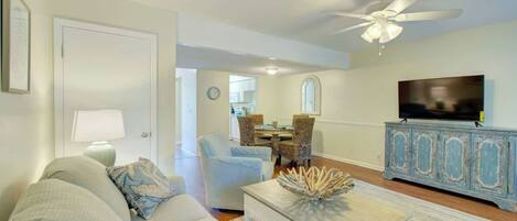 A living room with a sofa, a coffee table, a television, and a dining area with chairs and a table.