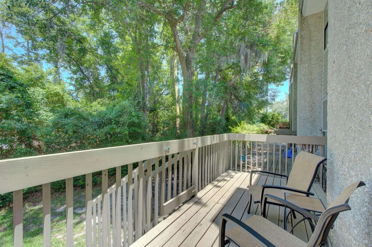A wooden deck with a railing, outdoor furniture, and a view of a forested area.